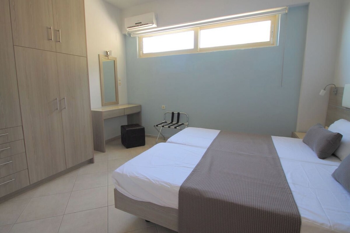 Een slaapkamer met een bed, een kledingkast, een spiegel, een bureau en een raam.