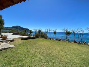 A grassy outdoor area with a view of the sea and mountains in the background.