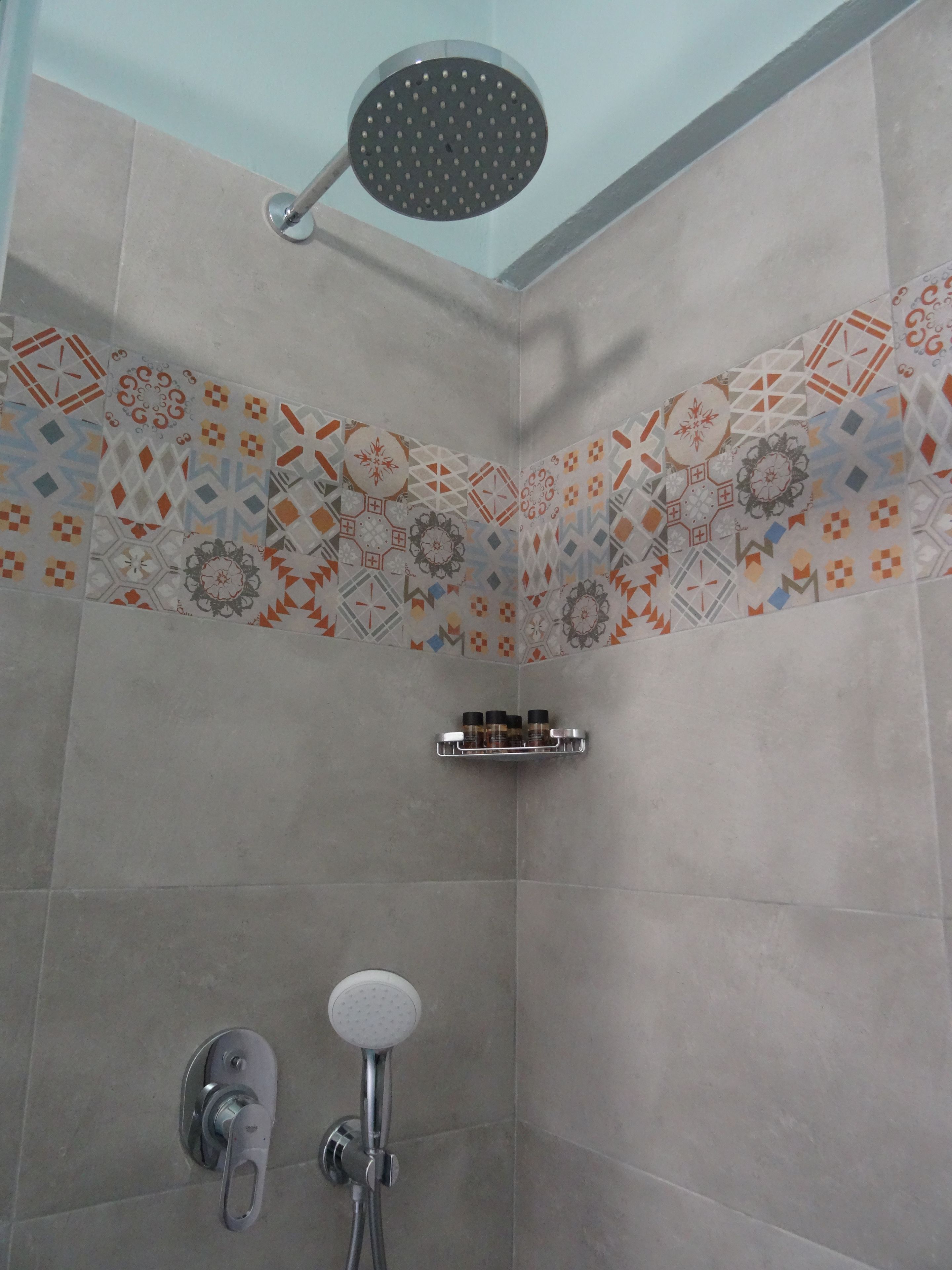 Ein Duschbereich mit Handbrause, fest installierter Brause und Ablage für Toilettenartikel.