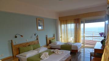 A hotel room with two beds, a wooden headboard design, a small table, and a view of the sea through large windows.