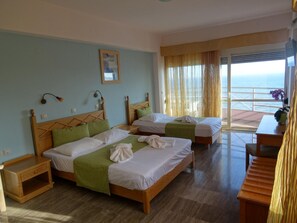 A hotel room with two beds, a wooden headboard design, a small table, and a view of the sea through large windows.