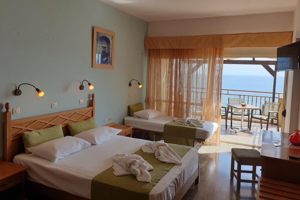 A hotel room with two beds, a balcony with a table and chairs, and a view of the sea.