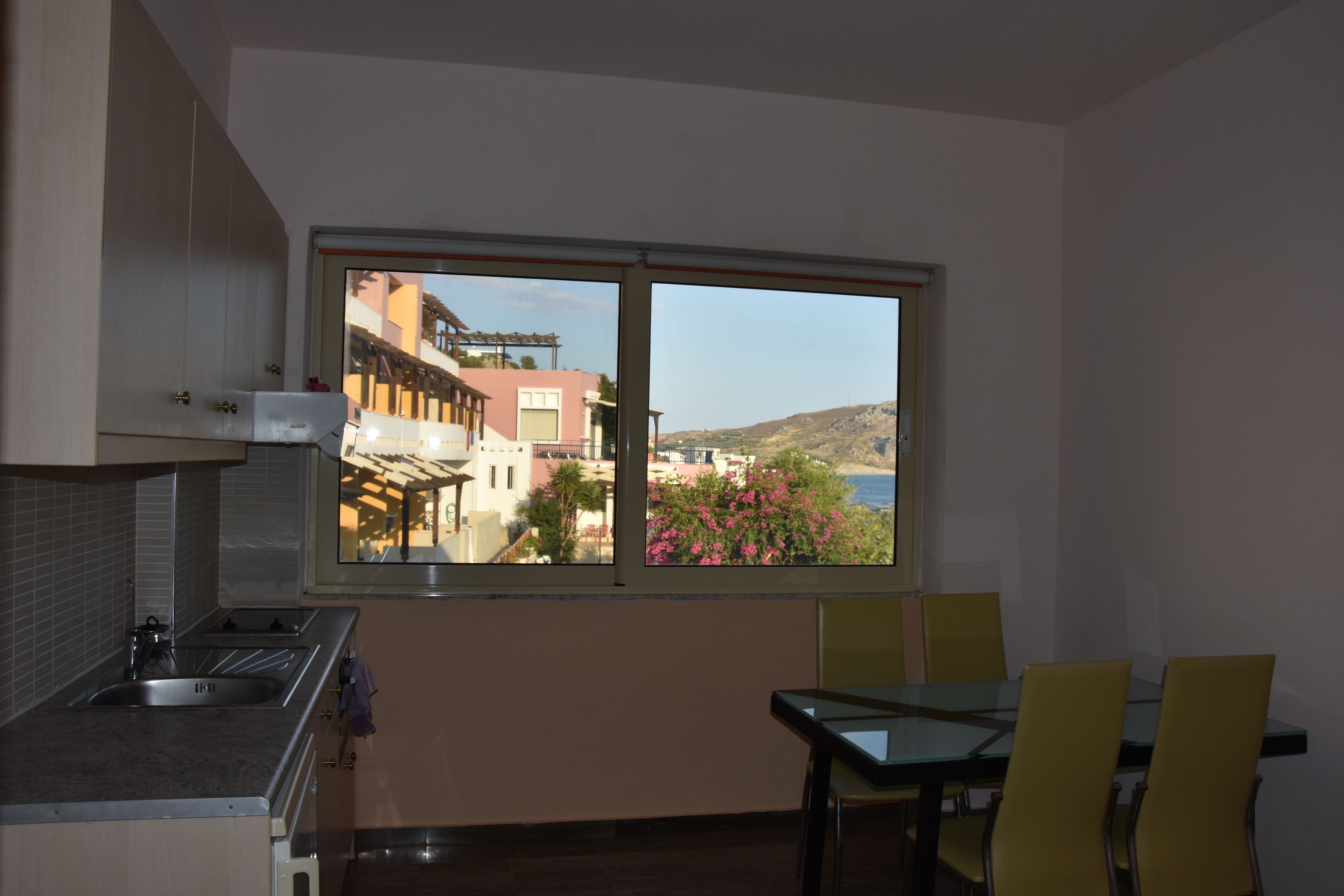Una cocina con ventana, una mesa de comedor con sillas y vistas a edificios y colinas.
