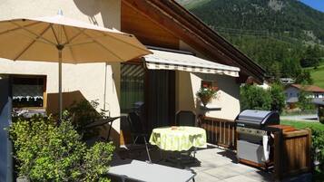 Eine Terrasse im Freien mit Tisch, Stühlen, einem Grill und einem großen Sonnenschirm.