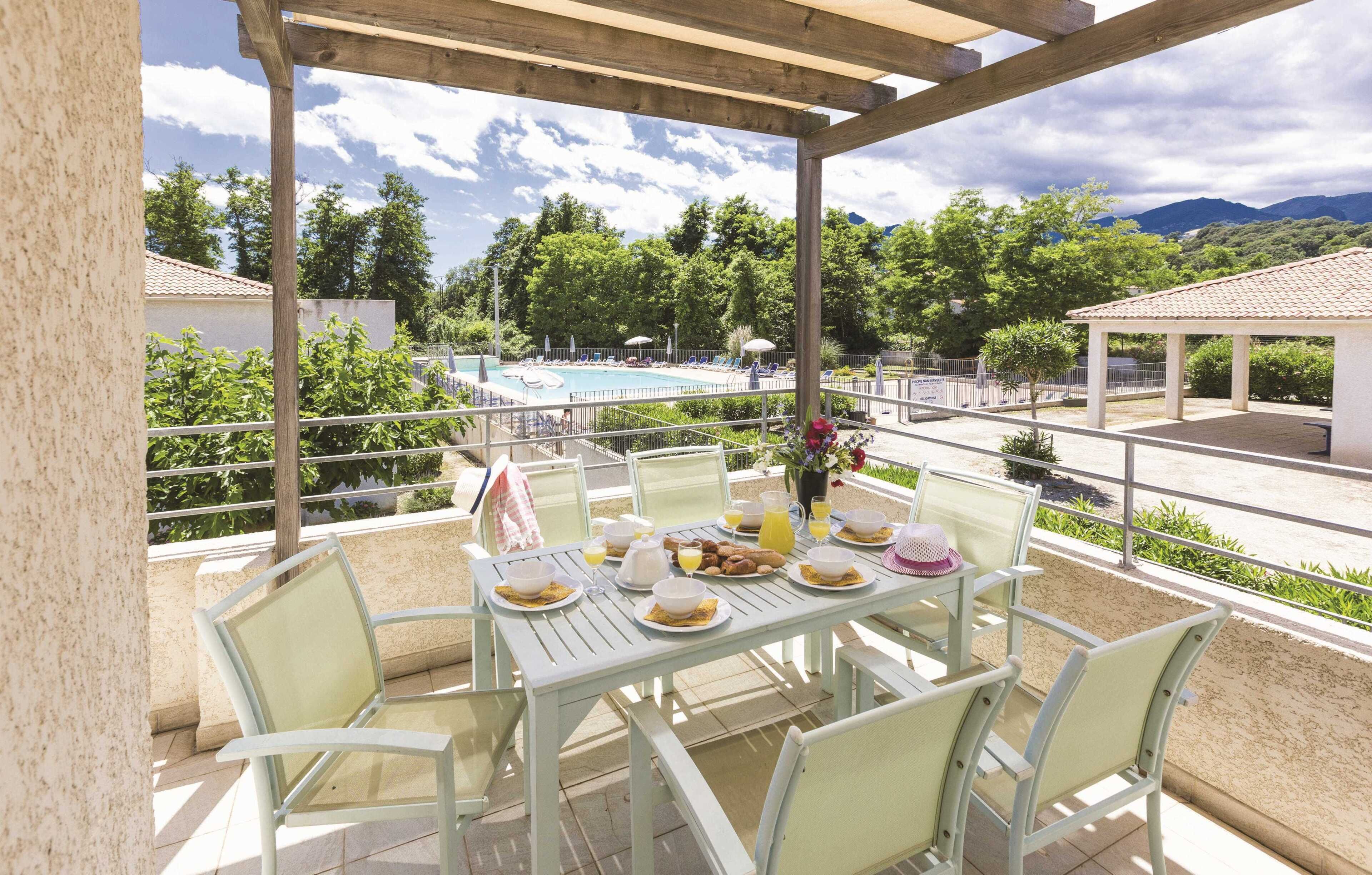Un espace extérieur abrité, aménagé pour prendre les repas, avec vue sur la piscine, des chaises blanches et une table dressée pour le petit-déjeuner.