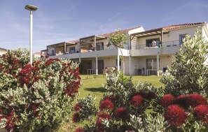 Un immeuble à plusieurs étages, doté de balcons, d’un toit plat et d’un jardin bien entretenu agrémenté de fleurs rouges.