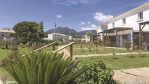 A residential area with houses, a grassy courtyard, and mountains in the background. - Residence Odalys Acqua Linda (Poggio-Mezzana)