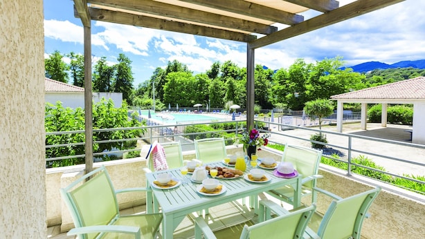 A covered outdoor dining area with a pool view, green chairs, and a table set for breakfast. - Residence Odalys Acqua Linda (Poggio-Mezzana)