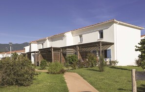 Un bâtiment blanc avec un toit recouvert de tuiles, un espace extérieur abrité et un chemin menant à l’entrée.