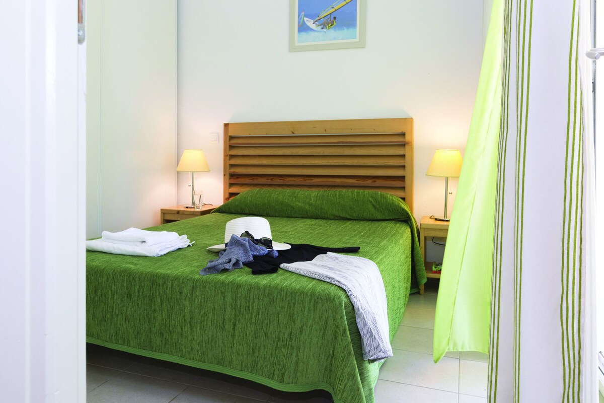 Une chambre avec un lit, deux lampes de chevet, un chapeau et des vêtements pliés posés sur le lit.