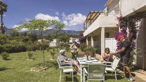 An outdoor dining area with a table set for four, surrounded by greenery and a mountain backdrop. - Residence Odalys Acqua Linda (Poggio-Mezzana)