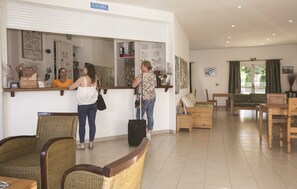 Un espace d’accueil avec des fauteuils en osier, un comptoir de réception et un espace d’attente doté de meubles en bois.