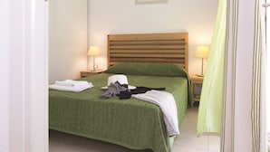 A neatly made bed with a green bedspread, two bedside lamps, and a framed picture on the wall. - Residence Odalys Acqua Linda (Poggio-Mezzana)
