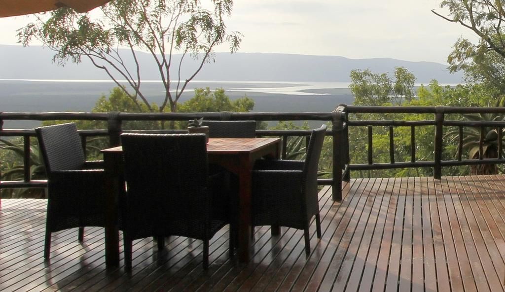 A wooden deck with outdoor furniture, a railing, and a view of a body of water and hills.