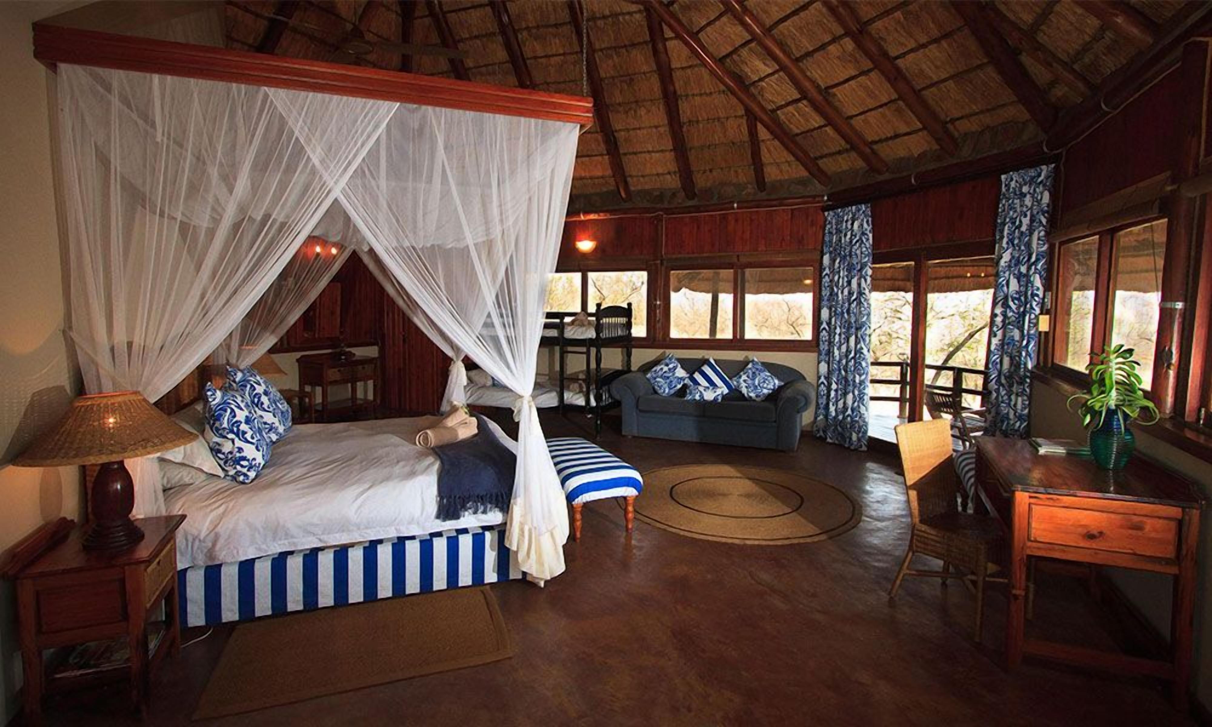 A room with a bed under a canopy, a sofa, a dining table, and a window with curtains.