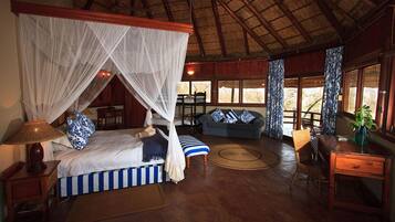 A room with a bed under a canopy, a sofa, a dining table, and a window with curtains.