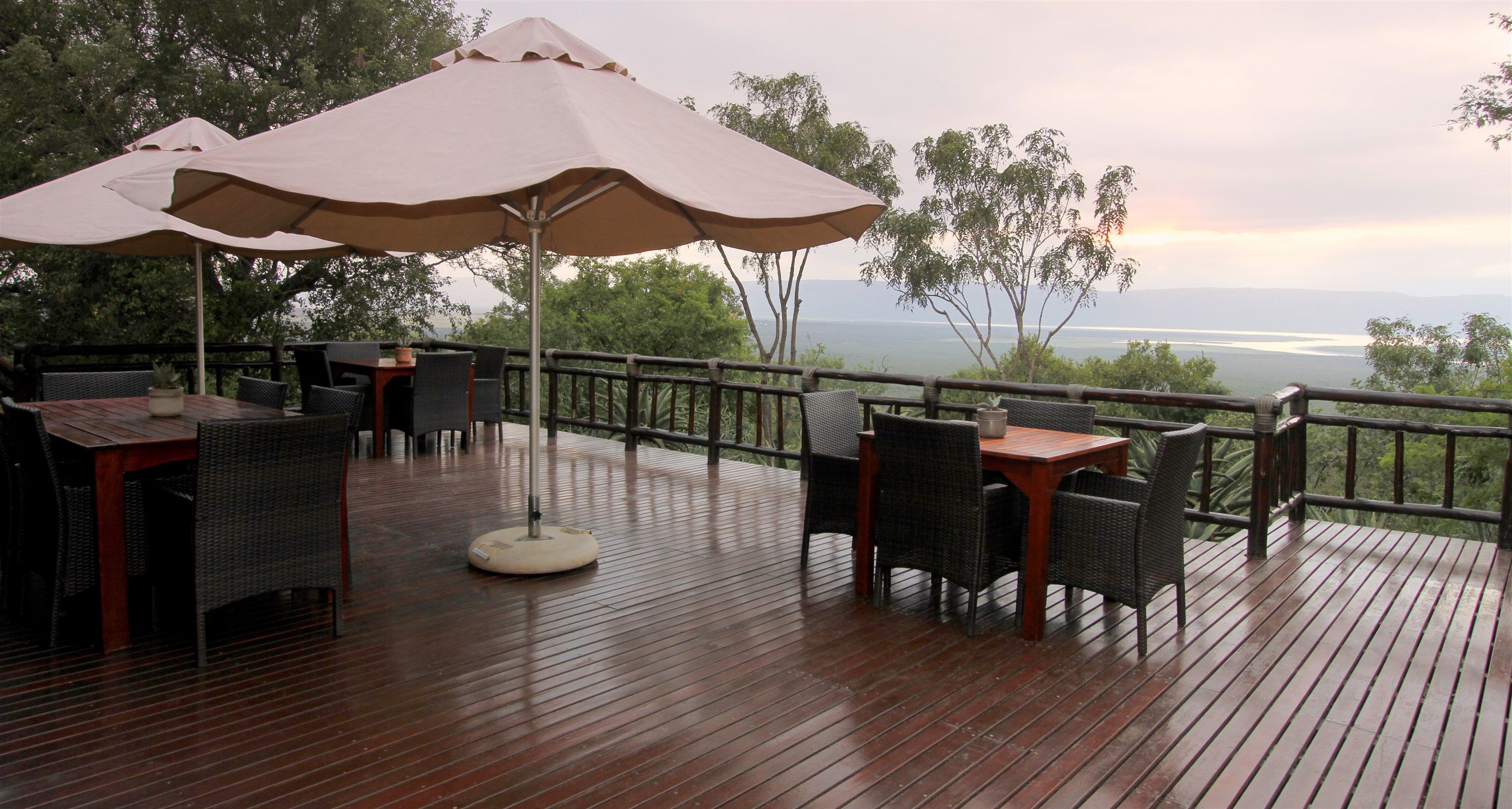 A wooden deck with outdoor seating, including tables and chairs, and large umbrellas providing shade.