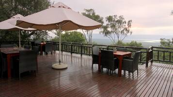 A wooden deck with outdoor seating, including tables and chairs, and large umbrellas providing shade.