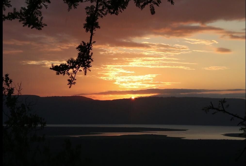 Un atardecer sobre un cuerpo de agua con siluetas de árboles y colinas distantes.