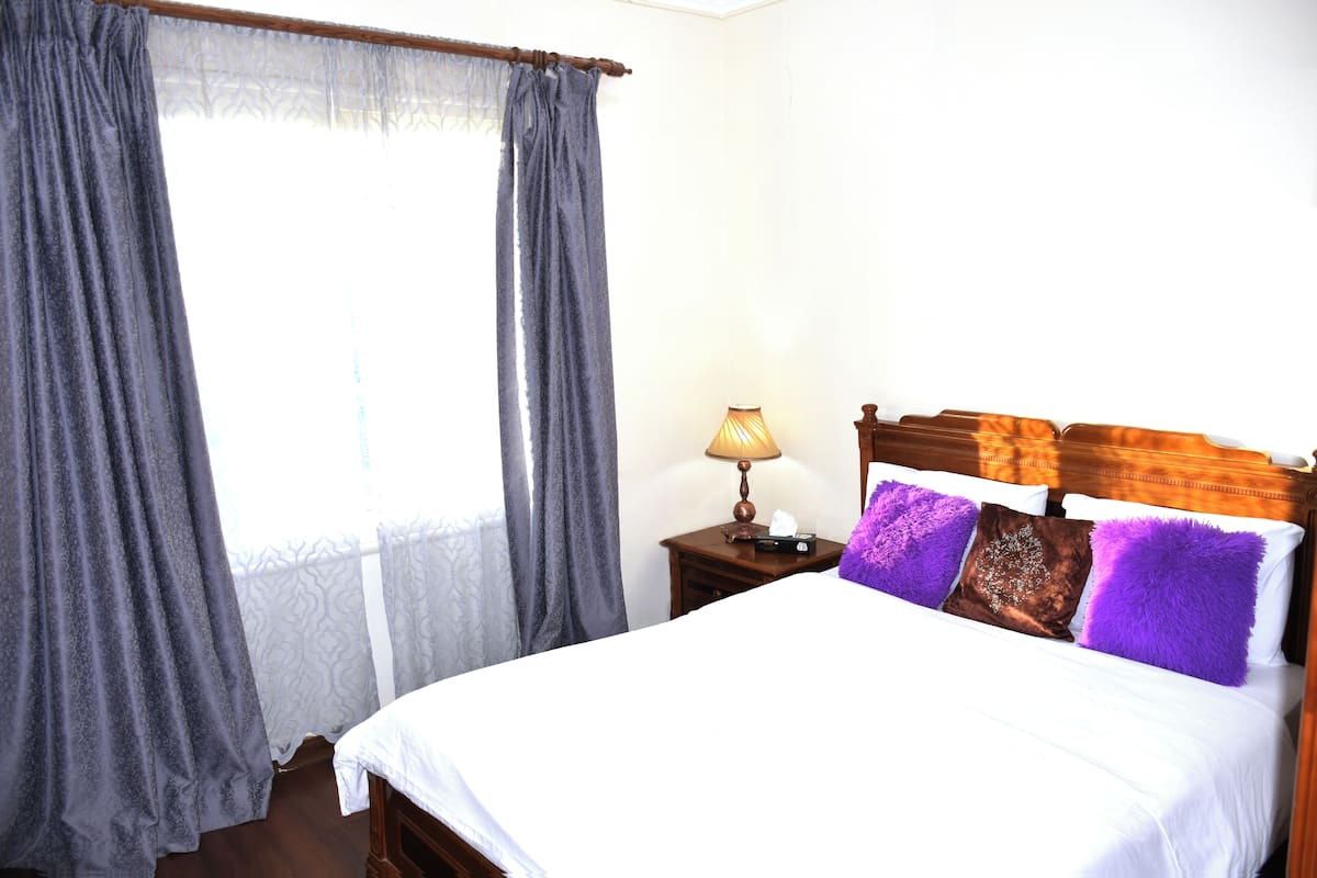 A bedroom with a bed, curtains, a nightstand, and a lamp.