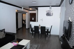 Uma sala de estar moderna com um sofá de couro preto, uma mesa de centro branca e uma área de jantar com mesa branca e cadeiras pretas.