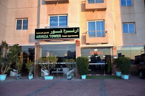 A hotel entrance with a sign reading 'ARINZA TOWER Hotel Apartments' and an 'ENTRANCE' sign. There are potted plants in front of the entrance. - Arinza Tower Quality Suites (Salmiya)