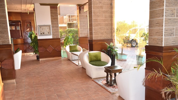 A lobby with a tiled floor, white sofas with green cushions, potted plants, and a reception desk. - Arinza Tower Quality Suites (Salmiya)