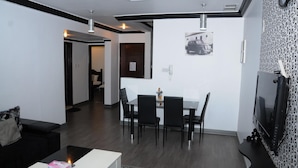 A modern living room with a black leather sofa, a white coffee table, and a dining area with a white table and black chairs. - Arinza Tower Quality Suites (Salmiya)