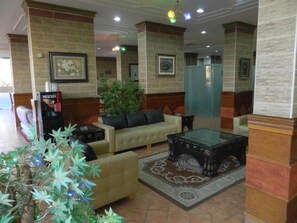 A lobby with a sofa, coffee machine, and a decorative plant. - Arinza Tower Quality Suites (Salmiya)