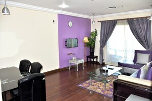 Uma sala de estar com parede roxa, um sofá, uma mesa de centro, uma TV e um espaço de jantar com cadeiras e uma mesa.
