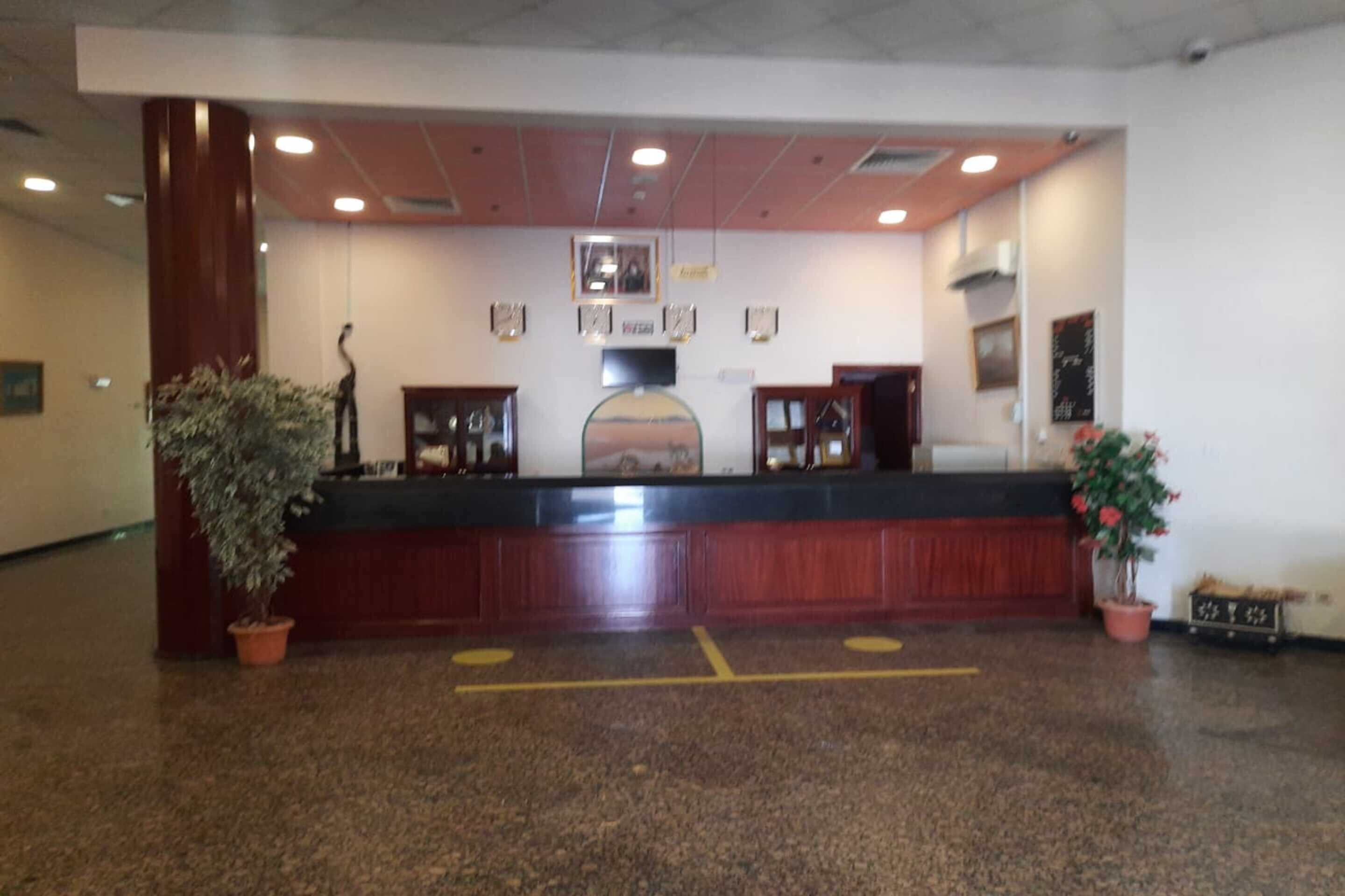 A reception area with a wooden reception desk, potted plants, and framed pictures on the wall.