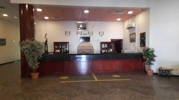 A reception area with a wooden reception desk, potted plants, and framed pictures on the wall.