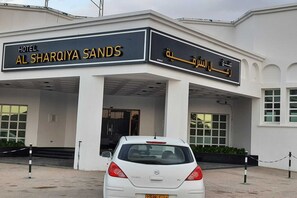The exterior of Hotel Al Sharqiya Sands with a white facade, a covered entrance, and a white car parked in front. - OYO 142 Al Sharqiya Sands Hotel (Ibra)