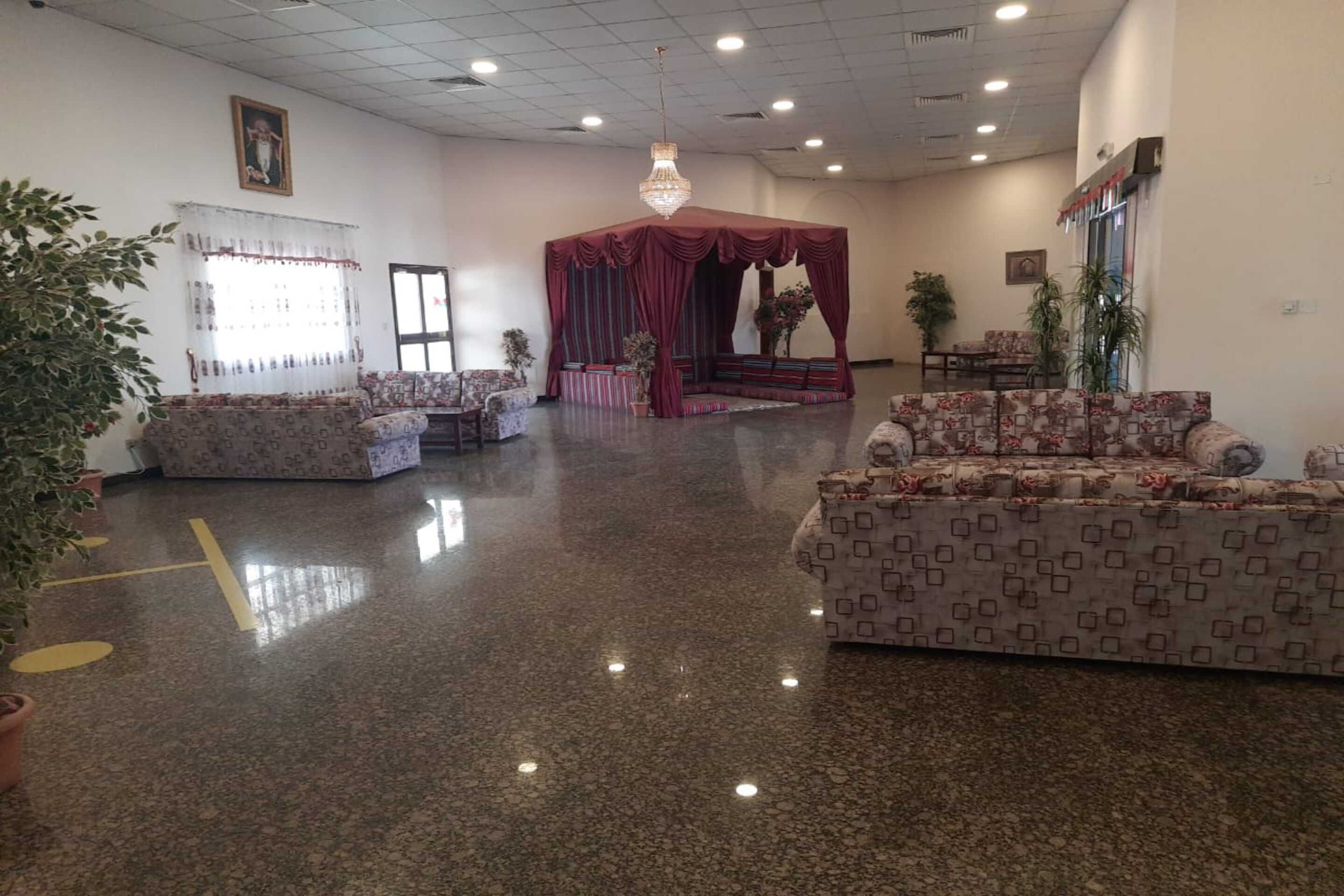 A spacious hotel lobby with a polished floor, patterned sofas, a red canopy seating area, and a chandelier.