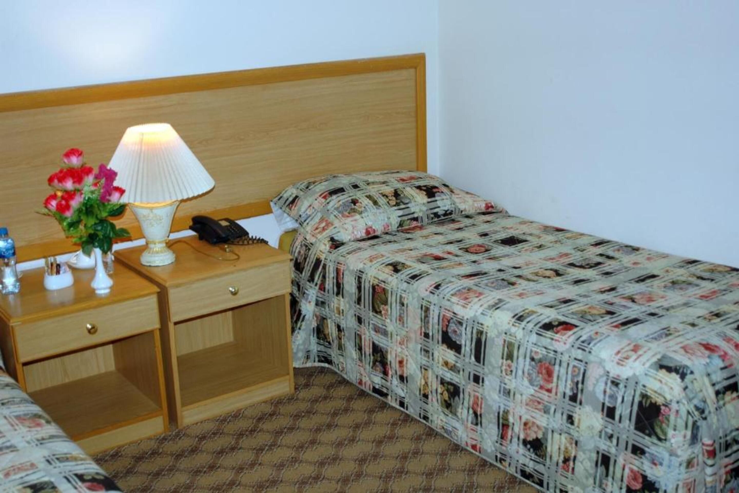 A hotel room with a wooden headboard, a bedside table with a lamp, a phone, and a floral arrangement.