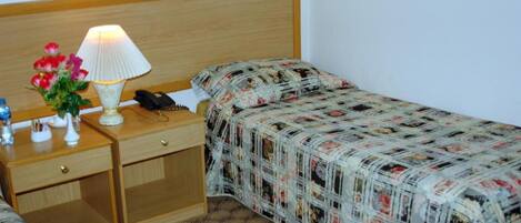 A hotel room with a wooden headboard, a bedside table with a lamp, a phone, and a floral arrangement.