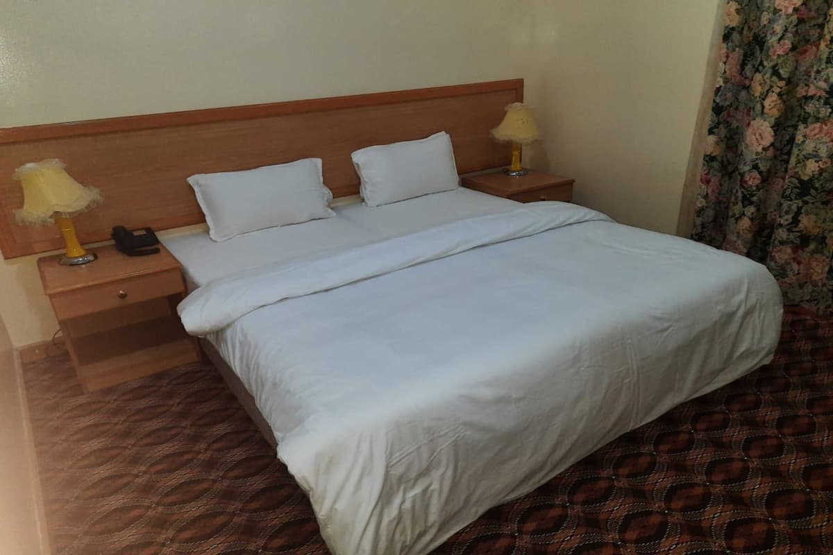 Quarto de hotel com uma cama, duas mesas de cabeceira, um telefone e uma luminária em cada mesa.