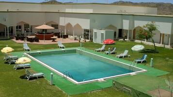 A swimming pool with lounge chairs and umbrellas, surrounded by a building with multiple doors and windows.