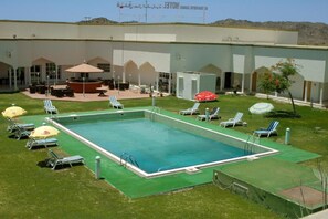 A swimming pool with lounge chairs and umbrellas, surrounded by a building with multiple doors and windows. - OYO 142 Al Sharqiya Sands Hotel (Ibra)