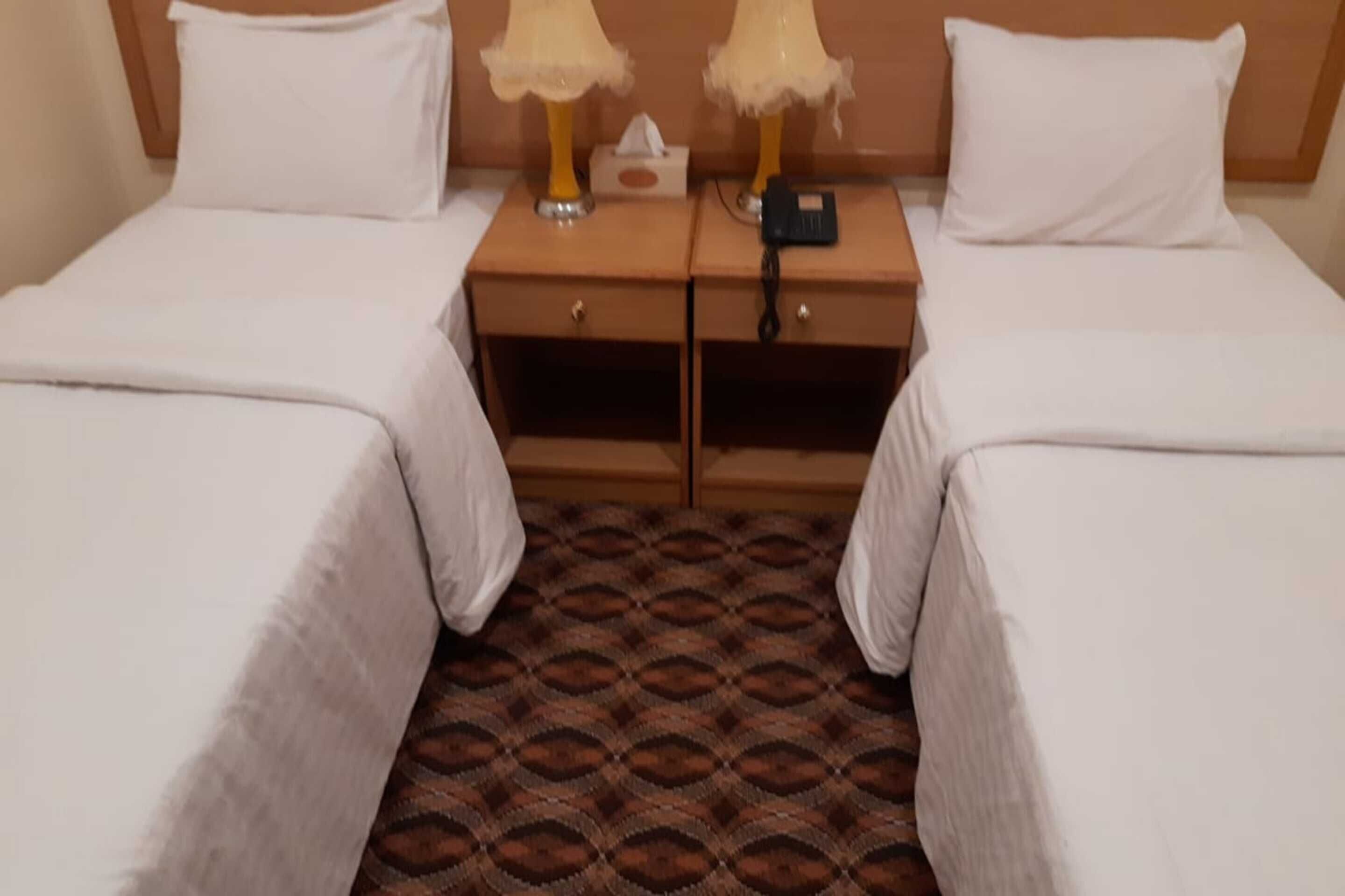 Een hotelkamer met twee enkele bedden, een houten nachtkastje ertussen, een zakdoosje en een oplader.