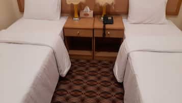 A hotel room with two single beds, a wooden nightstand between them, a tissue box, and a phone charger.