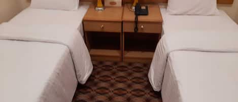 A hotel room with two single beds, a wooden nightstand between them, a tissue box, and a phone charger.