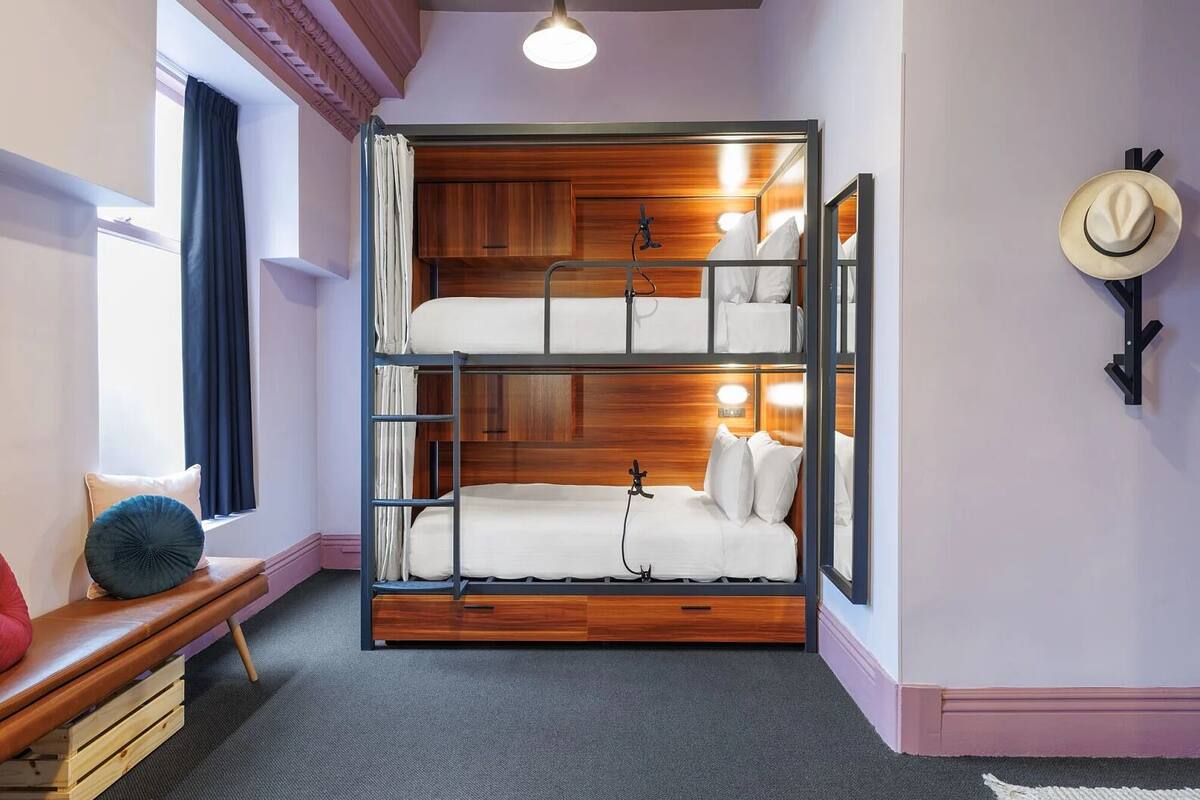 A bunk bed room with a wooden headboard, a bedside lamp, and a mirror on the wall.