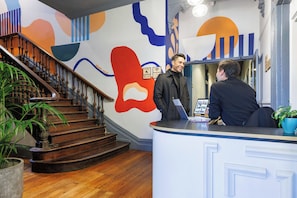 A reception desk with a modern design, a staircase with wooden steps, and a decorative wall with abstract patterns. - Selina St Kilda Melbourne (Melbourne)