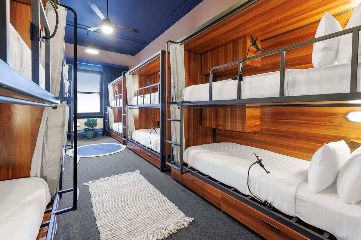 A bunk room with wooden headboards, a ceiling fan, and a window with curtains.