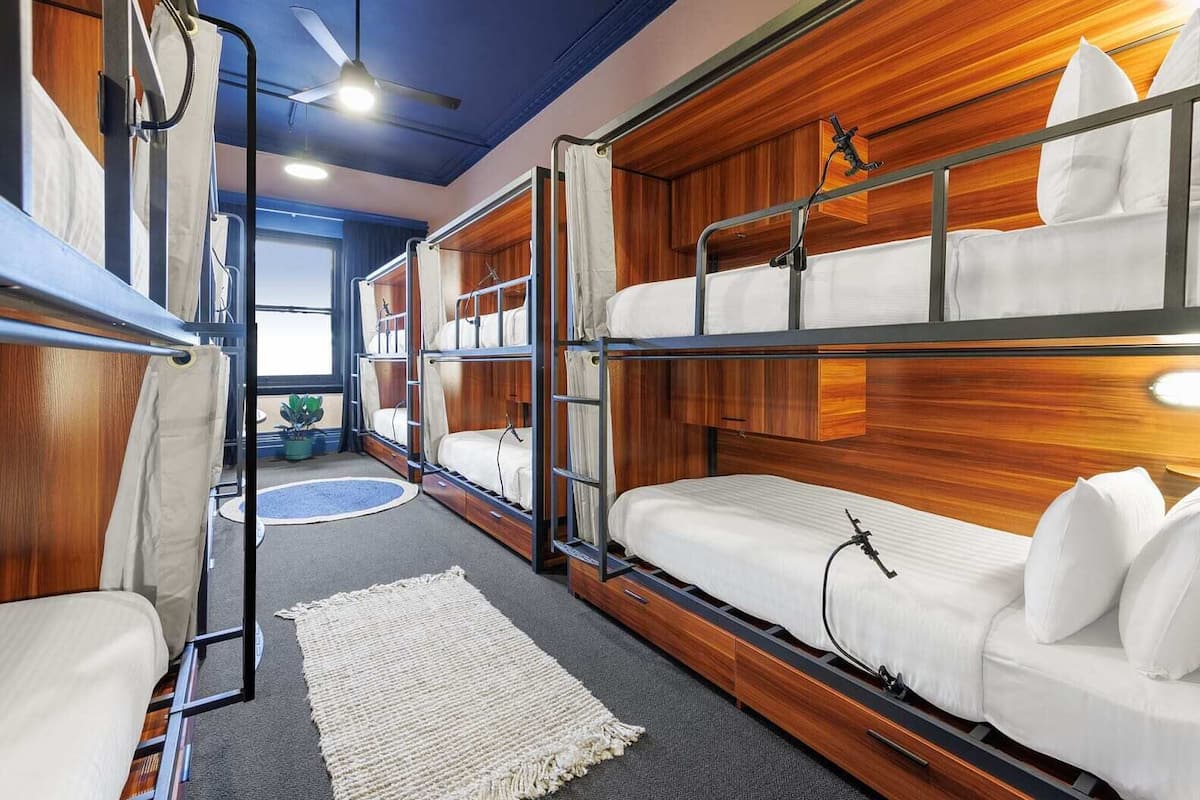 A bunk room with wooden headboards, a ceiling fan, and a window with curtains.