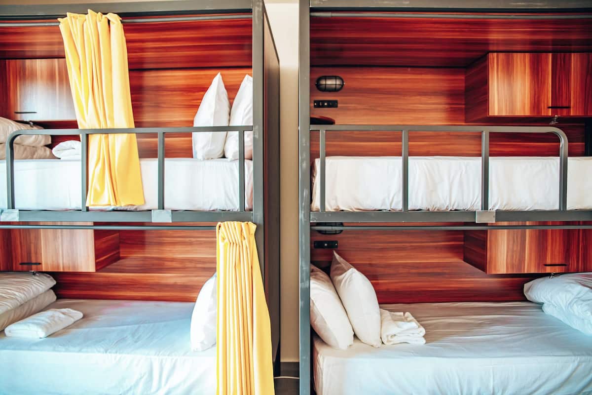 A hotel room with bunk beds, wooden headboards, and a small bedside table with a lamp.