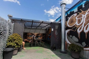 A covered outdoor area with a metal roof, potted plants, and a mural on the wall. - Selina St Kilda Melbourne (Melbourne)