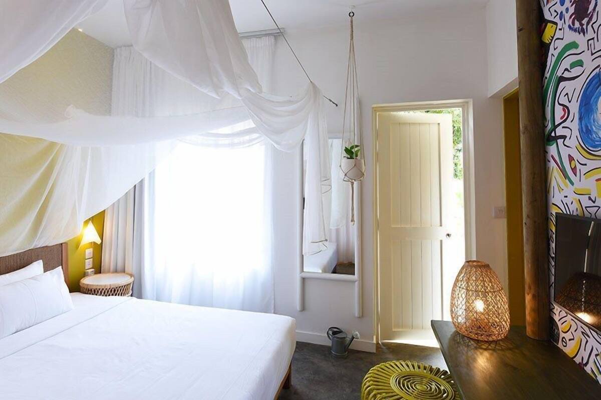 A bedroom with a bed, a hanging chair, a small table with a plant, and a door leading to another room.