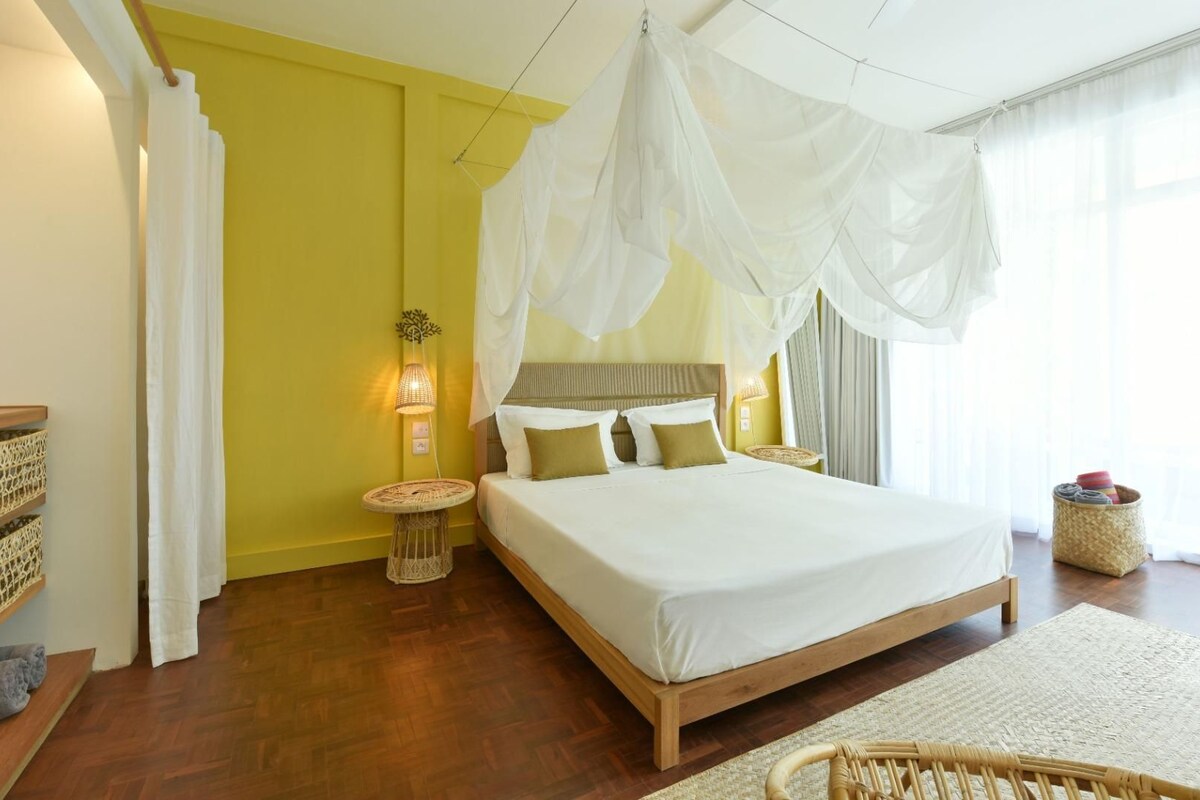 Un dormitorio con cama, mesitas de noche, lámpara y ventana con cortinas.